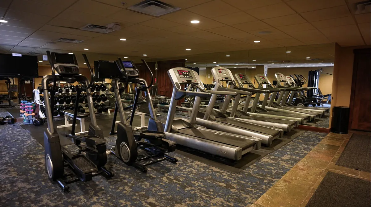 The image features a well-equipped fitness center filled with treadmills, ellipticals, dumbbells, and mirrors. The space is designed to encourage group activities and social fitness, evoking a sense of energetic camaraderie. The clean, modern gym vibe hints at the resort’s lively, communal atmosphere, inviting guests to enjoy active experiences together.