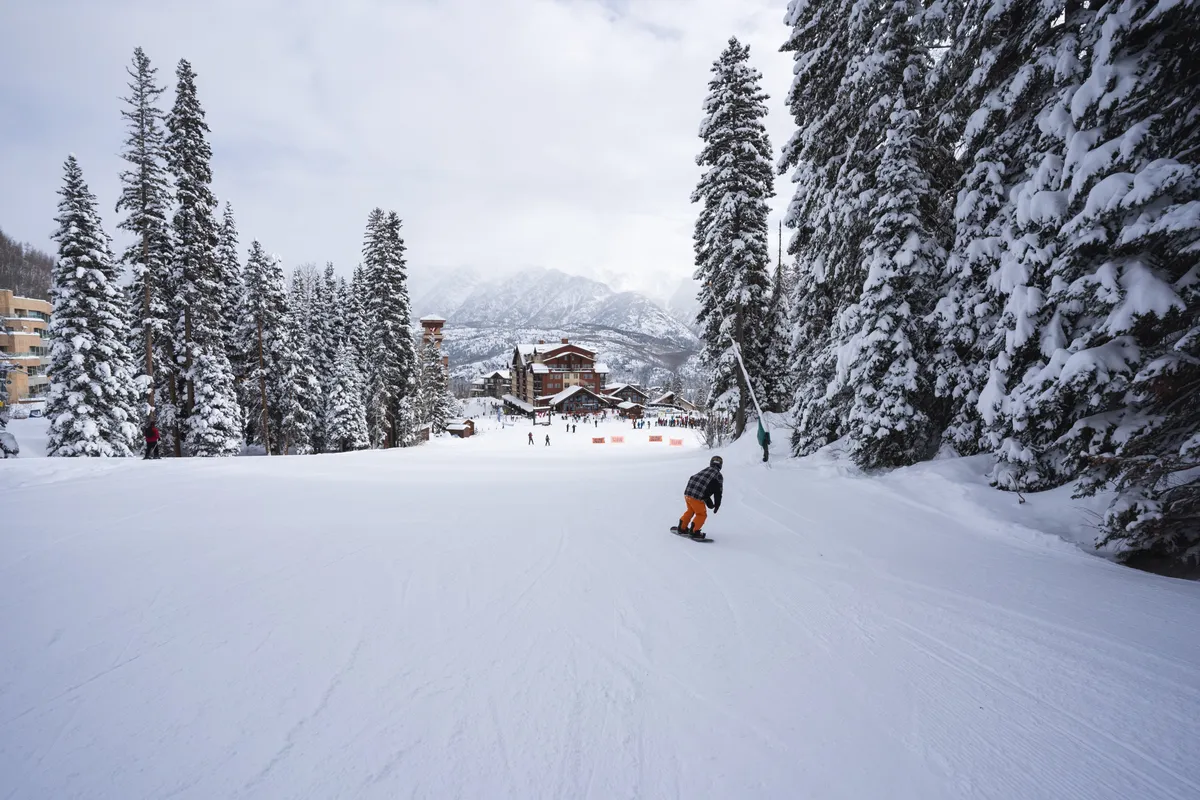 An action-packed exterior view featuring a snowboarder carving through fresh snow, surrounded by snow-covered trees and resort buildings. The energy and excitement of winter sports are palpable, highlighting the adventure available just outside.