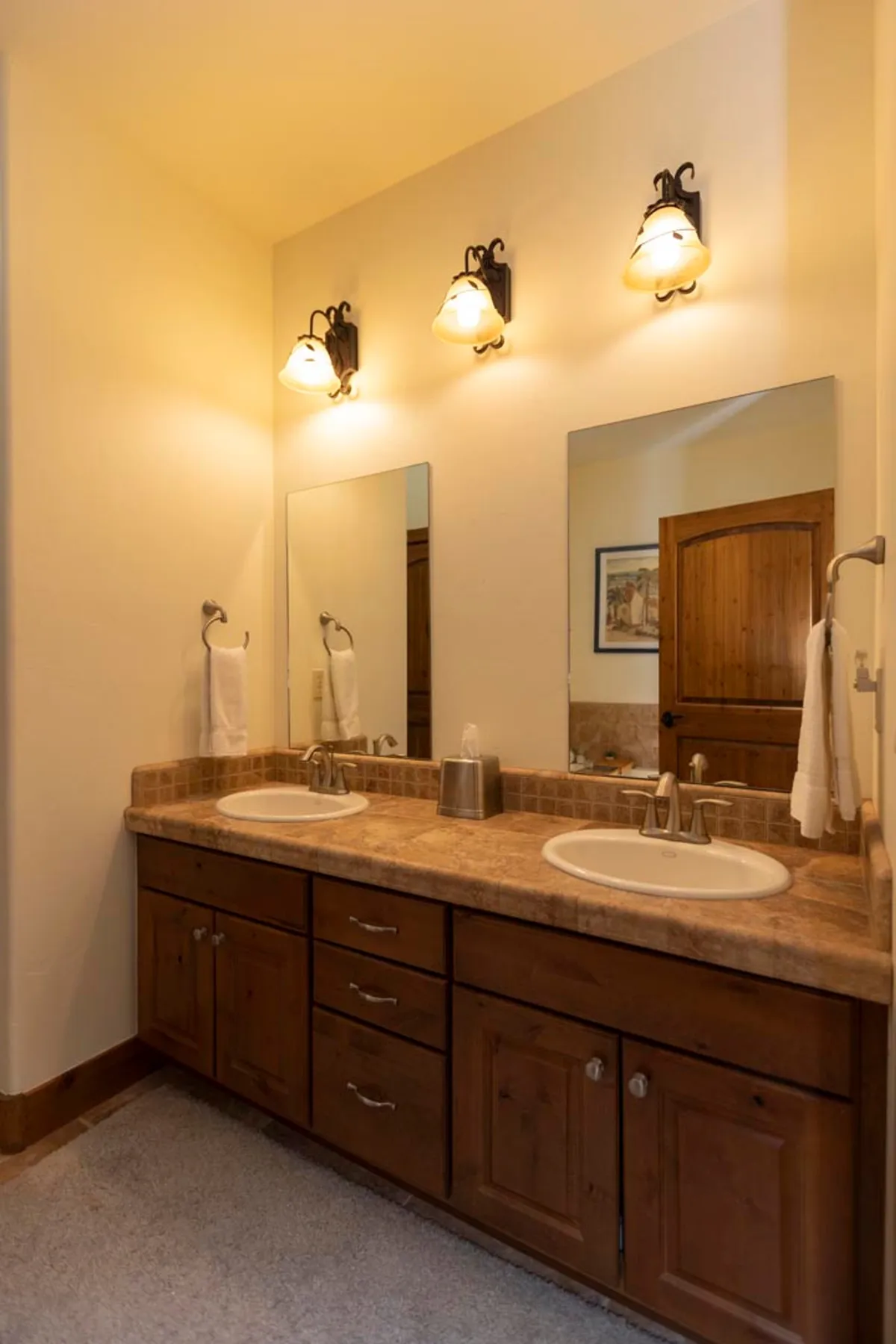 A modern bathroom with double sinks set in a wooden vanity, topped by large framed mirrors and illuminated by task lighting. The room feels calm and organized, perfect for self-care and preparing for a day’s adventures.