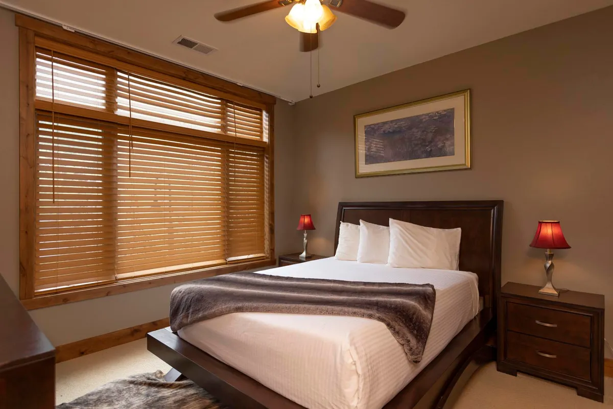 A second bedroom scene showcasing a comfortable bed flanked by stylish nightstands and lamps, with art adorning the walls. Soft daylight streams in through a window, creating an inviting and restful mood ideal for unwinding.